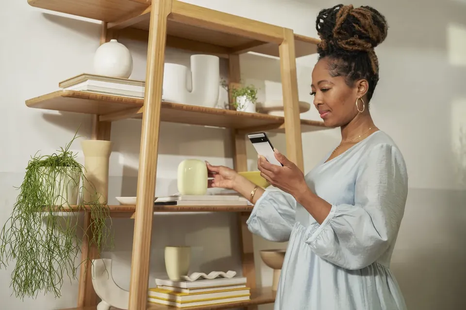 Google Nest Wifi Pro on a shelf beside a person using a phone